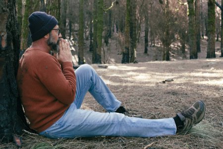 Téléchargez les photos : Homme ayant du temps de détente assis sur le sol au milieu de forêts verdoyantes et activités de loisirs de détente en plein air. Les gens et l'amour sentiment avec le parc naturel. Bien-être mode de vie alternatif - en image libre de droit