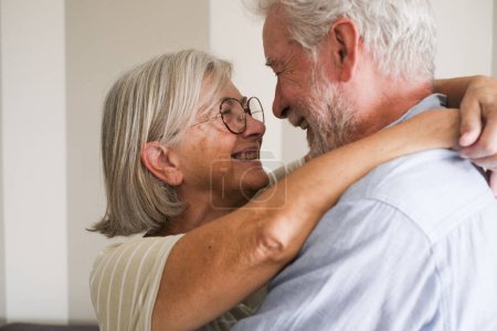 Ältere Liebe mit einem kaukasischen reifen Paar, das sich umarmt und einander lächelnd und liebevoll in den Augen sieht. Senioren verbinden sich und genießen Freizeitaktivitäten im Innenraum mit Romantik