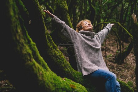 Foto de Mujer feliz en la actividad de ocio al aire libre. Celebrando el estilo de vida saludable y la libertad. El día de la Tierra. Mujer sentada y extendiendo los brazos en el bosque con árboles verdes en el fondo. Bosque - Imagen libre de derechos