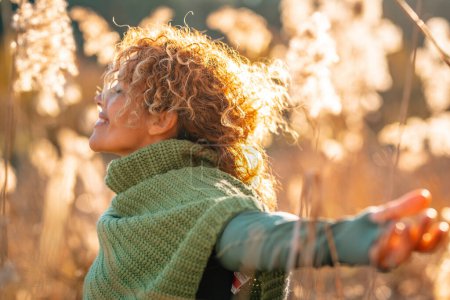 Happy serene adult woman hug outstretching arms in the nature outdoor leisure activity. Joyful female people opening arms in a golden field during sunset light. Nature lover. Happiness mental health