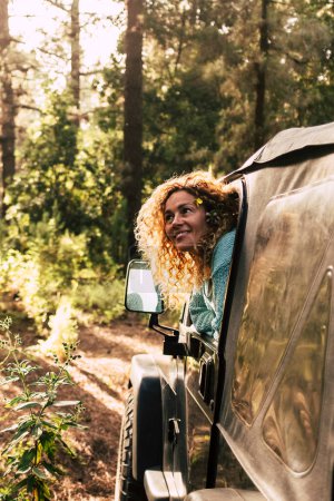 Foto de Turismo alternativo la gente descubre la naturaleza con un coche todoterreno disfrutando del bosque y la madera a la luz del sol puesta del sol - alegre mujer feliz fuera del vehículo dentro del bosque - Imagen libre de derechos