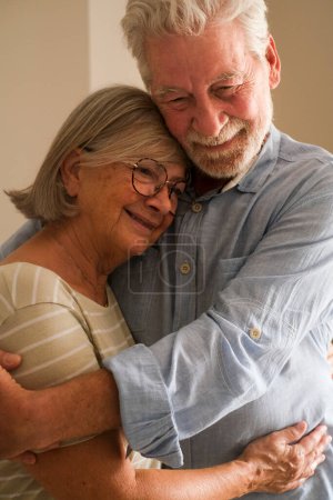 Téléchargez les photos : Soins aux personnes âgées couple mature étreignant et rêvant ensemble à la maison. senior homme et femme se lient en souriant. Amour heureux et relation personnes âgées style de vie activités de loisirs en intérieur - en image libre de droit