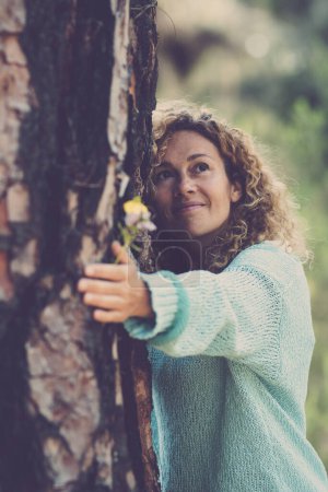 Photo for Serene woman hugging tree trunk in the forest smiling and looking at the woods around. People in love for nature. Outdoors environmental leisure activity. Healthy natural lifestyle people. Happy lady - Royalty Free Image