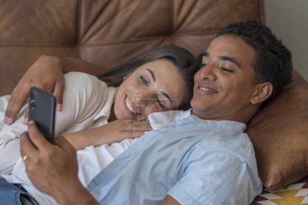 Side view of romantic young boy and girl having relax and love laying on the sofa in indoor lazy leisure activity together. Real life and modern lifestyle people. Interracial relationship people.
