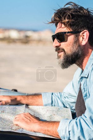 Photo for Handsome mature man outside the car using paper guide map on car hood. Bearded adult male people enjoy travel lifestyle and looking for roads to drive alone. Traveler lifestyle. Alternative vacation - Royalty Free Image