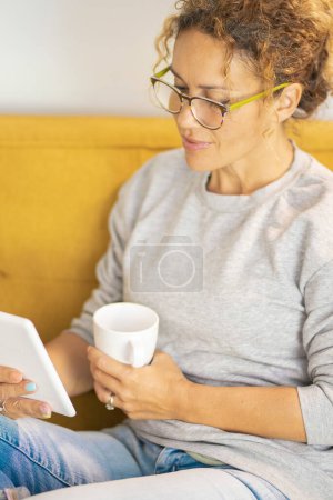 Woman in indoor leisure relaxation activity alone read and use electronic tablet reader device to read new ebook from online library. People and wireless connection at home. Relax lifestyle female
