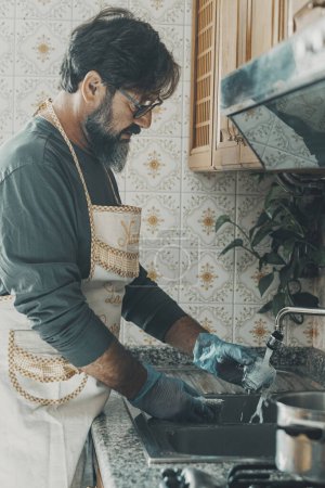 Foto de Hombre lavar los platos en casa en la cocina después de la hora del almuerzo. Esposo ayudando a su esposa a limpiar la casa. Rutina doméstica de limpieza de apartamentos interiores. Concepto de personas que viven solas y trabajo doméstico - Imagen libre de derechos