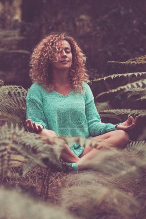 Photo for Life balance nature contact feeling serene woman doing meditation in lotus yoga posture position. Happiness and relaxation in the forest sitting with tropical leaf around. People outdoor leisure relax - Royalty Free Image