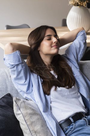 relaxed person smiling sitting on a couch in the living room at home with a window 