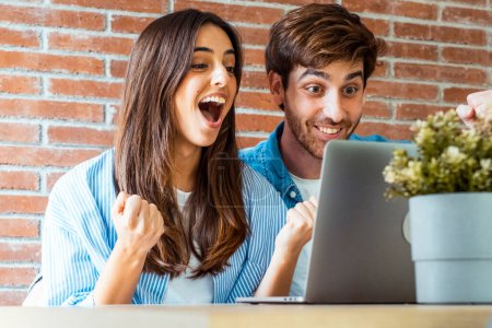Téléchargez les photos : Jeune couple adulte devant un ordinateur portable avec gagnant excité expression joyeuse et geste ensemble. - en image libre de droit