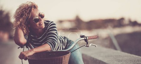 Foto de Woman smile and enjoy outdoor leisure activity alone having relax on her bike. Happy female people smile and look wearing sunglasses. Healthy transport lifestyle people sustainability - Imagen libre de derechos