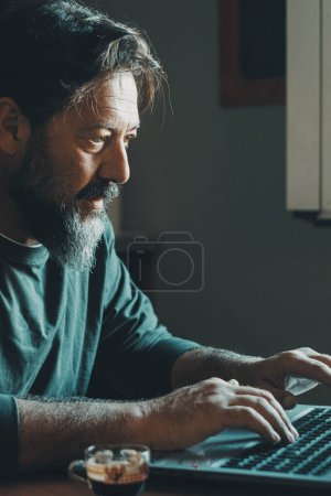 Photo for Mature male workaholic involved in work overtime, type report letter on laptop, search data at web. Ambitious young man in smart working develop career spend free time on computer at home alone indoor - Royalty Free Image