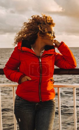 Photo for Woman smile alone admiring sunset color on the outside dock of a ferry boat. Transport and travel holiday vacation. Female people enjoying outside leisure activity on the ship. Sky in background - Royalty Free Image