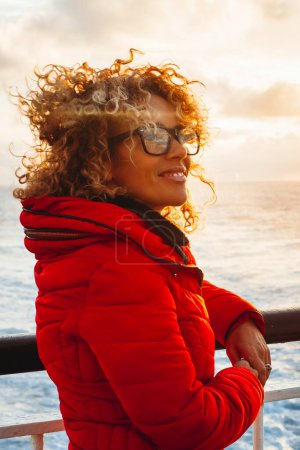 Photo for Cruise ship vacation woman enjoying sunset on travel at sea. Traveler happy woman in red jacket looking at ocean relaxing on luxury cruise liner boat. People and ferry boat transport. Travel activity - Royalty Free Image