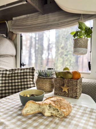 Foto de Interior de autocaravana caravana con comida en la mesa y vista al bosque fuera de la ventana. Concepto de vanlife y gente de viaje estilo de vida vacacional - Imagen libre de derechos