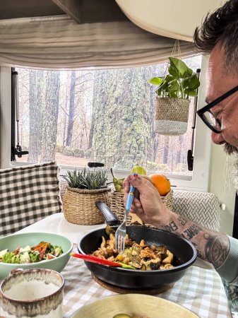 Photo for Man eating alone inside a camper van with forest woods  outside the window. Travel people lifestyle. Living the vanlife. Nomadic vacation. Eating healthy inside a motorhome - Royalty Free Image