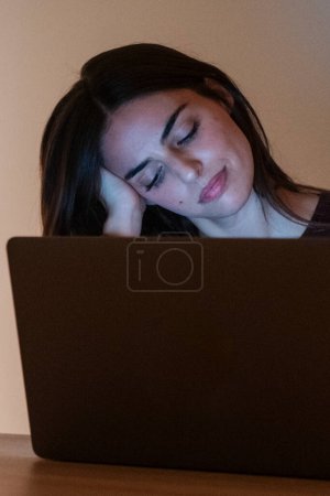Junge hübsche lächelnde Frau mit Laptop zu Hause in der Nacht. Glückliches Mädchen beim Blick auf den Computer. Fröhliche Menschen sitzen am Schreibtisch im Wohnzimmer. Konzept des unternehmungslustigen und fleißigen Menschen.
