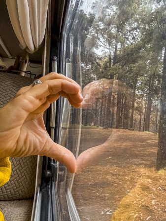 Photo for Woman puts her hand on the glass forming a heart with the reflection. Concept of play and love for nature - Royalty Free Image
