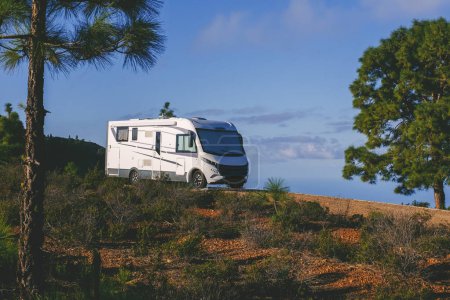 Modern motorhome camper van parking in the nature with trees and mountains around for free park camping alternative garden home and destination for holiday vacation. Living alone off grid traveler