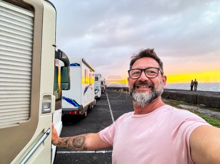 Un hombre feliz tomando foto selfie en el lado de una caravana moderna autocaravana. Viajero vanlife estilo de vida personas que comparten en las redes sociales aventura y viaje. Increíble puesta de sol en el fondo. Aparcamiento