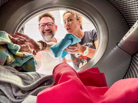 couple doing laundry View from the inside of washing machine.Happy adult man and woman cleaning and washing clothes together in homework or business activity. Using laundromat