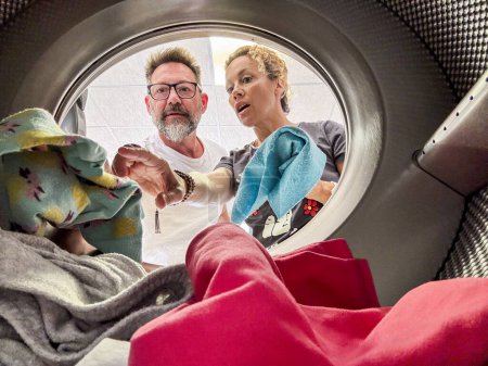Photo for Couple doing laundry View from the inside of washing machine.Happy adult man and woman cleaning and washing clothes together in homework or business activity. Using laundromat - Royalty Free Image