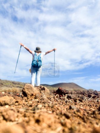 Foto de Senderismo mujer persona visto desenfocado desde atrás con la mochila levantando los brazos y disfrutar de la caminata destino solo sobre un fondo de cielo azul. Concepto de actividad de ocio al aire libre - Imagen libre de derechos