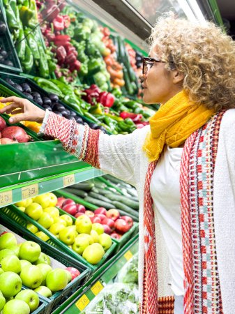 Foto de Retrato de primer plano, hermosa, bonita mujer joven en suéter recoger, la elección de verduras de hoja verde en la tienda de comestibles - Imagen libre de derechos