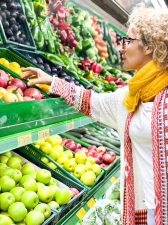 Foto de Hermosa joven comprando frutas y verduras en el departamento de productos de una tienda de comestibles / supermercado (imagen tonificada en color) - Imagen libre de derechos