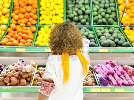 Photo for Beautiful young woman shopping for fruits and vegetables in produce department of a grocery store/supermarket (color toned image) - Royalty Free Image