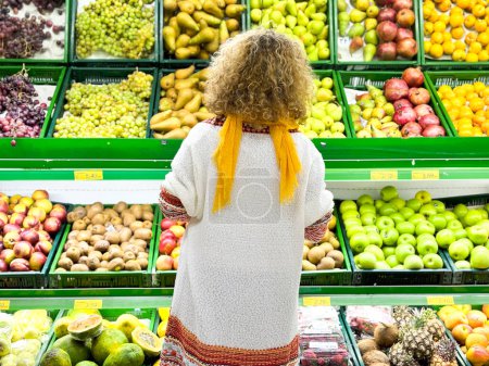 Téléchargez les photos : Vue arrière du bouclé Belle jeune femme faisant du shopping pour des fruits et légumes dans le département des produits d'une épicerie / supermarché (image tonique de couleur) - en image libre de droit
