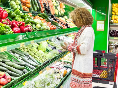Téléchargez les photos : Belle jeune femme faisant du shopping pour les fruits et légumes dans le département des produits d'une épicerie / supermarché (image tonique de couleur) - en image libre de droit