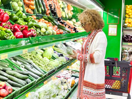Téléchargez les photos : Gros plan portrait, belle, jolie jeune femme en pull ramassant, en choisissant des légumes verts à feuilles dans l'épicerie - en image libre de droit