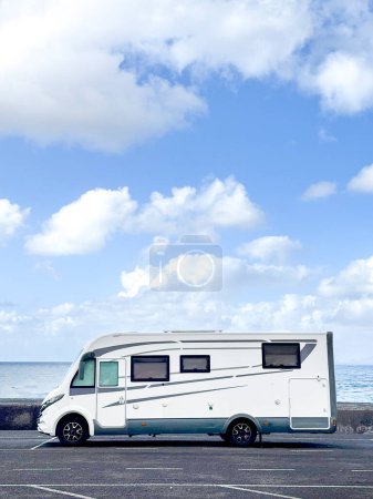 modern motorhome parking on the asphalt against a blue ocean and sky. Concept of travel and living off grid people.