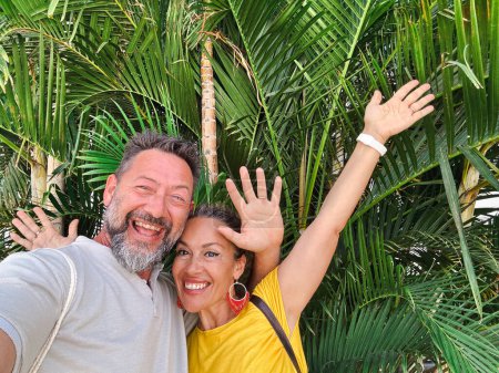 Téléchargez les photos : Couple adulte prenant des photos selfie avec des feuilles de parc vert en arrière-plan souriant et s'amusant devant la caméra du téléphone. Style de vie touristique gens concept. Loisirs - en image libre de droit
