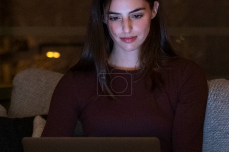 Portrait of young happy woman using laptop at night, using modern technology having fun with glowing screen in dark office or at home, startup business meeting online with businesswoman