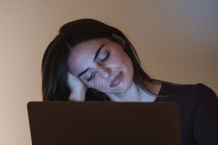 Junge hübsche lächelnde Frau mit Laptop zu Hause in der Nacht. Glückliches Mädchen beim Blick auf den Computer. Fröhliche Menschen sitzen am Schreibtisch im Wohnzimmer. Konzept des unternehmungslustigen und fleißigen Menschen.