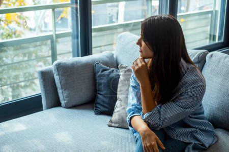 Depressed young woman sitting on couch in the living room at home, Frustrated confused female feels unhappy problem