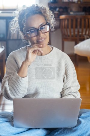 Photo for Middle age lady sitting on the floor comfortable using laptop at home in indoor technology wireless leisure activity alone. Modern female people working on computer. Woman browsing web and writing - Royalty Free Image