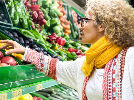 Foto de Retrato de cerca, hermosa, mujer bonita en suéter recoger, la elección de verduras de hoja verde en la tienda de comestibles - Imagen libre de derechos