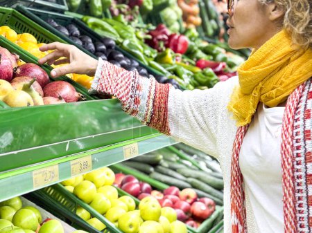 Téléchargez les photos : Belle femme faisant du shopping pour les fruits et légumes dans le département des produits d'une épicerie / supermarché (image tonique de couleur) - en image libre de droit