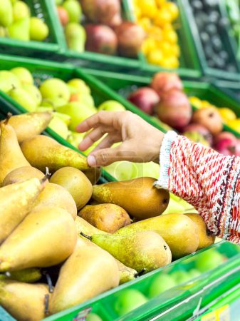 Foto de Primeros planos mano femenina tomando frutas en el mercado, hermosa, mujer bonita en suéter recoger, la elección de verduras de hoja verde en la tienda de comestibles - Imagen libre de derechos