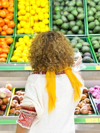 Foto de Vista trasera de rizado Hermosa joven comprando frutas y verduras en el departamento de productos de una tienda de comestibles / supermercado (imagen tonificada en color) - Imagen libre de derechos
