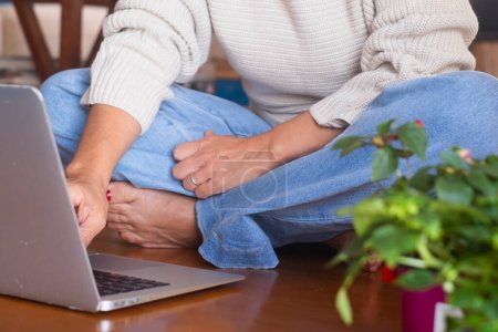 Téléchargez les photos : Femme d'âge moyen assis sur le sol confortable en utilisant un ordinateur portable à la maison dans la technologie d'intérieur activité de loisirs sans fil seul. Des femmes modernes qui travaillent sur ordinateur. Femme naviguant sur le web et écrivant - en image libre de droit