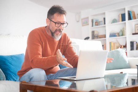 Photo for Smiling senior man wear glasses gesturing to camera having video call on laptop, happy adult male enjoy computer connection sit on couch at home talk using modern technologies and wireless connection - Royalty Free Image