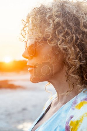 Photo for Side portrait of curly cute woman with sunset sunlight in background in outdoor leisure activity alone. Attractive long hair female people adult in contemplation. People lifestyle. Cute lady. - Royalty Free Image