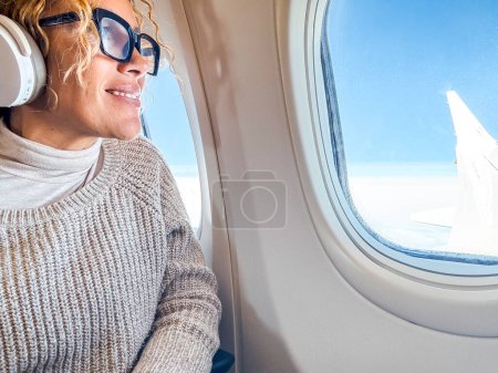 Foto de Viajes y vacaciones. .. Atractiva mujer de mediana edad escucha música y se relaja mientras está sentada en un cómodo asiento de avión - Imagen libre de derechos