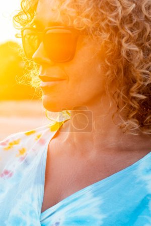 Photo for Funny outdoor portrait of curly young woman smiling and wearing sunglasses with sunset backlight. Golden portrait of attractive lady in outdoors leisure activity alone. Tourist happy. Beautiful female - Royalty Free Image