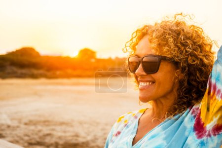 Photo for Funny outdoor portrait of curly young woman smiling and wearing sunglasses with sunset backlight. Golden portrait of attractive lady in outdoors leisure activity alone. Tourist happy. Beautiful female - Royalty Free Image