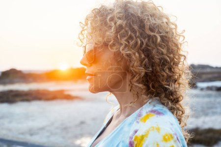 Photo for Side portrait of curly cute woman with sunset sunlight in background in outdoor leisure activity alone. Attractive long hair female people adult in contemplation. People lifestyle. Cute lady. - Royalty Free Image